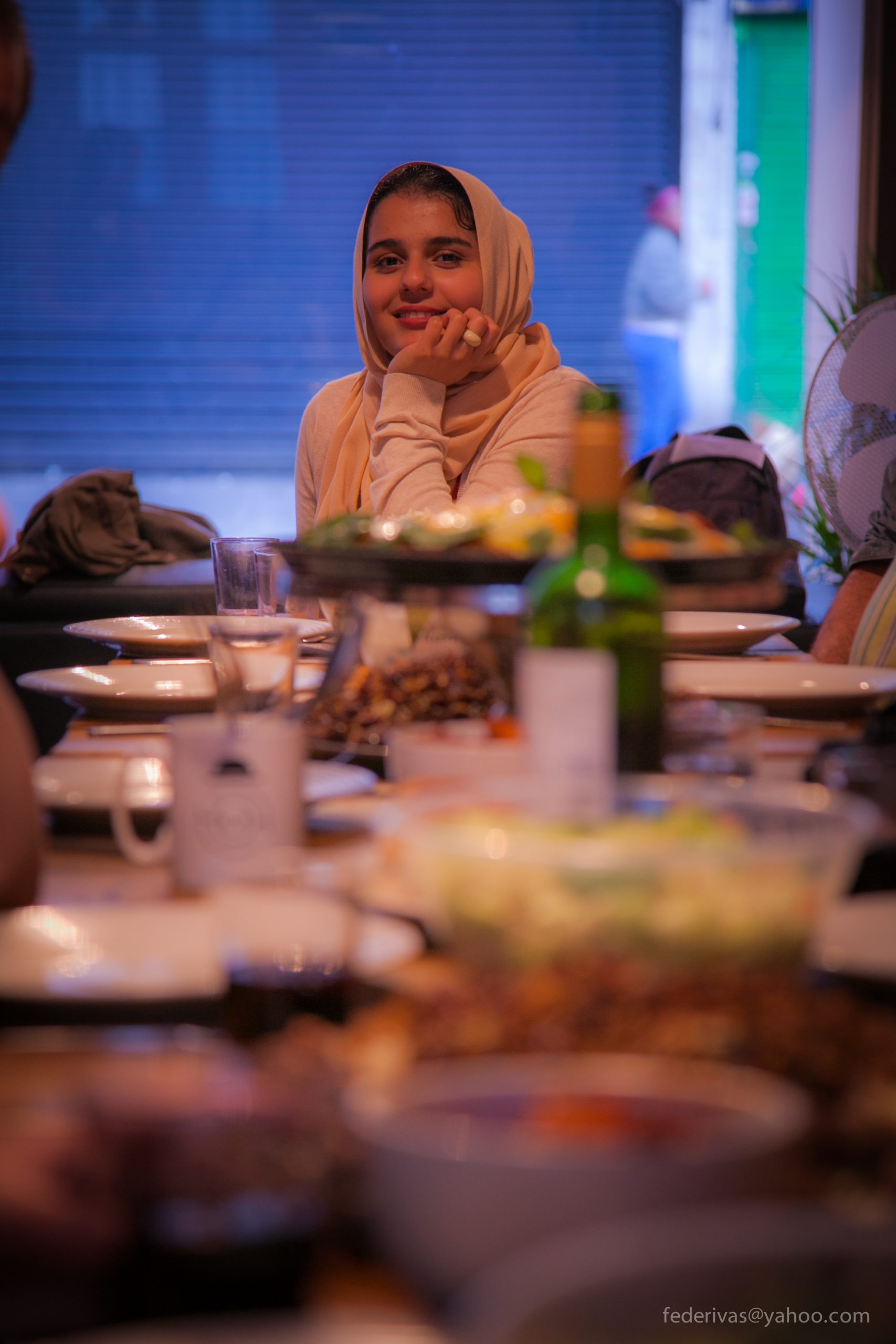 A woman wearing a hijab sitting at a table during a Migrateful London Cookery Class.