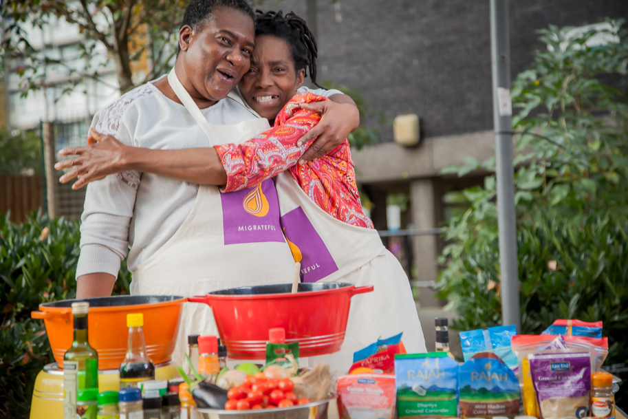 Two women participating in a London Cookery Class, hugging in front of a table full of food.