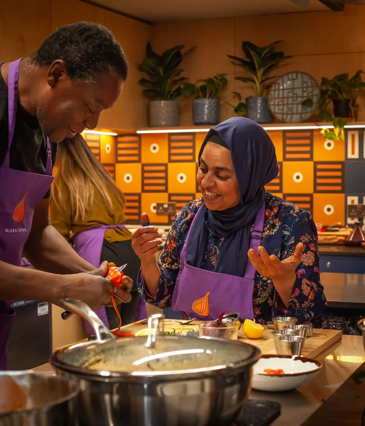Two people participating in a Migrateful London Cookery Class and preparing food in a kitchen.
