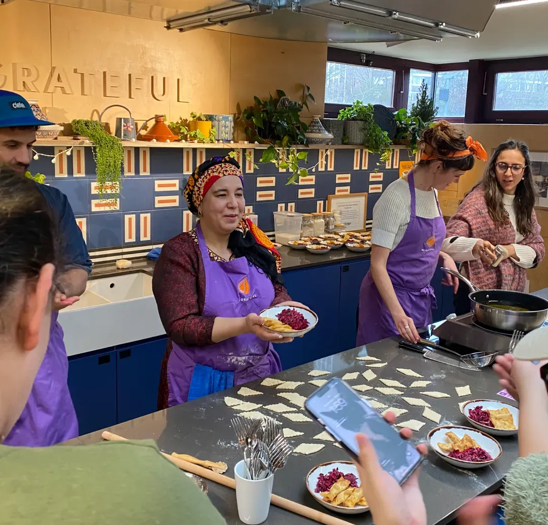 A group of people participating in a Migrateful London Cookery Class, preparing food together in a kitchen.