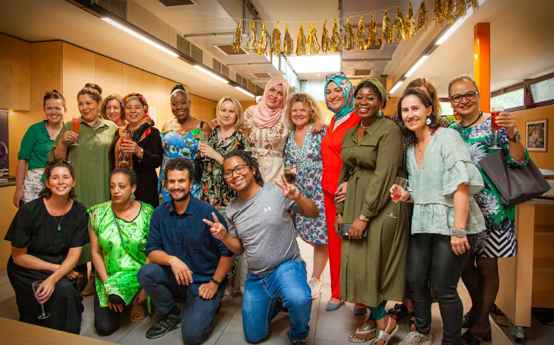 A group of people participating in a London Cookery Class and posing for a photo in an office organized by Migrateful.