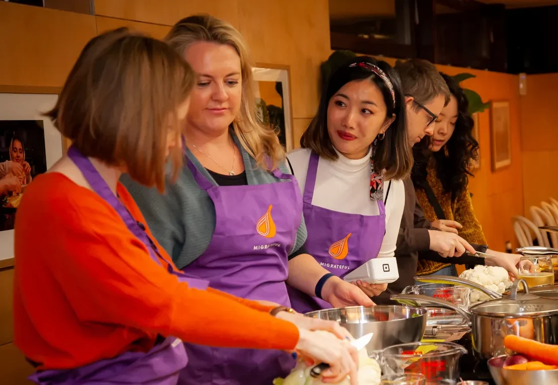 A group of women in purple aprons participating in a London Cookery Class organized by Migrateful.