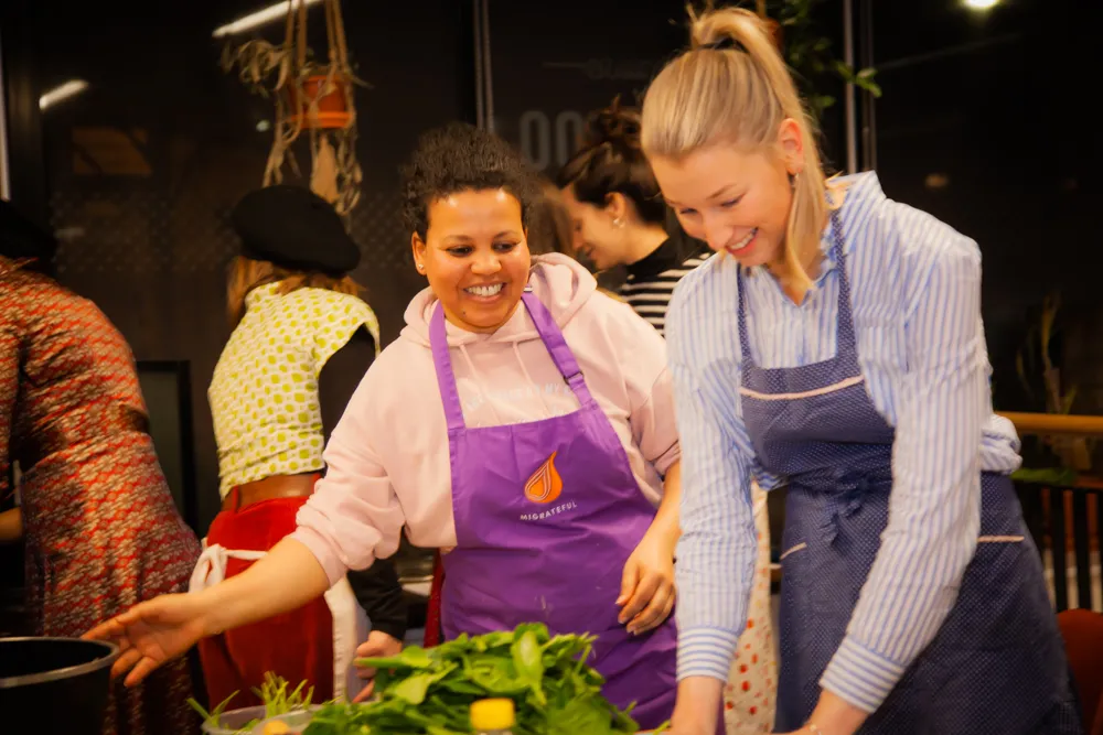 A group of women are preparing food in a kitchen at a Migrateful London Cookery Class.