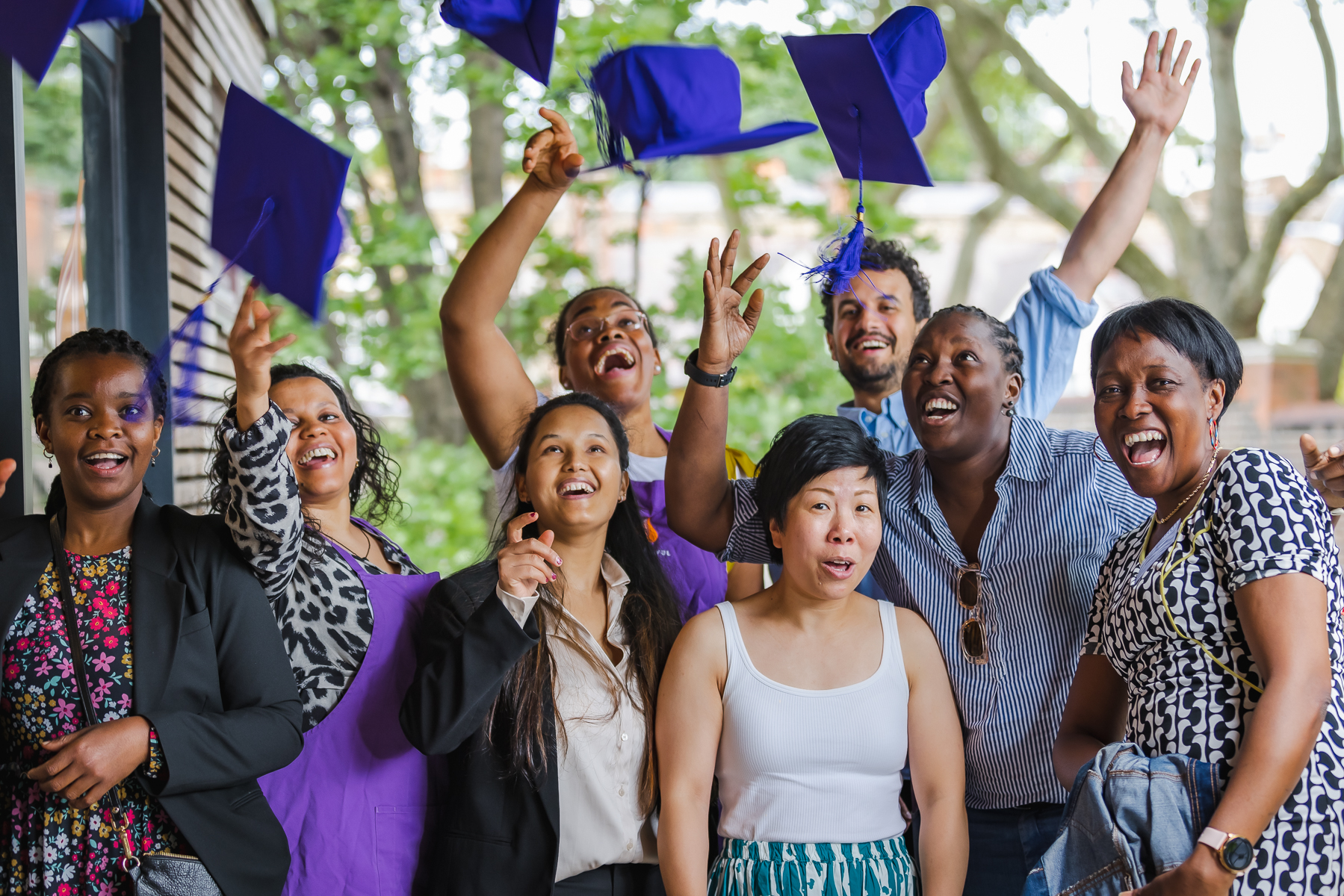 A group of people with graduation hats in the air, celebrating their completion of a Migrateful London Cookery Class.