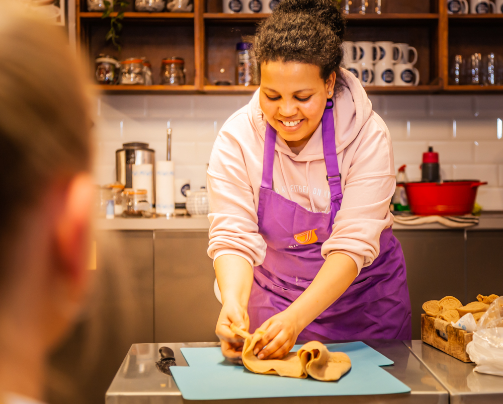 A woman wearing a purple apron, participating in a London Cookery Class organized by Migrateful.