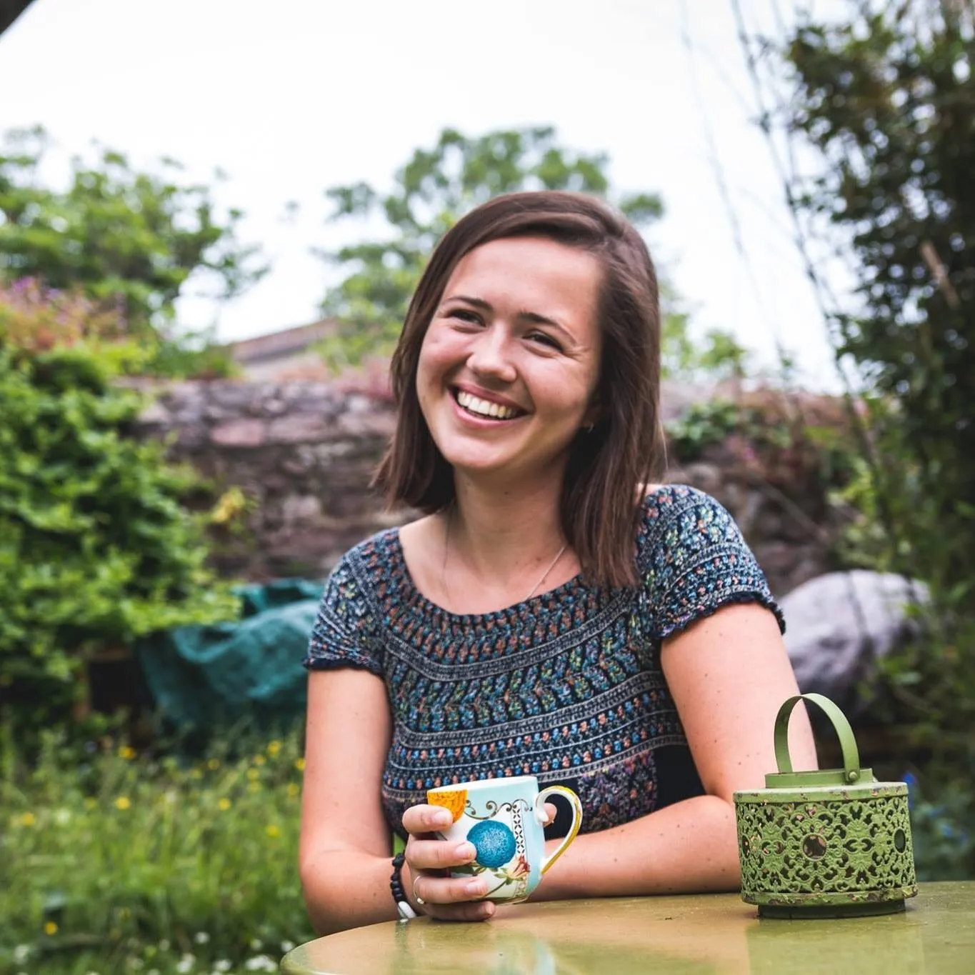 A woman smiles while sitting at a table in a Migrateful London Cookery Class in a garden.