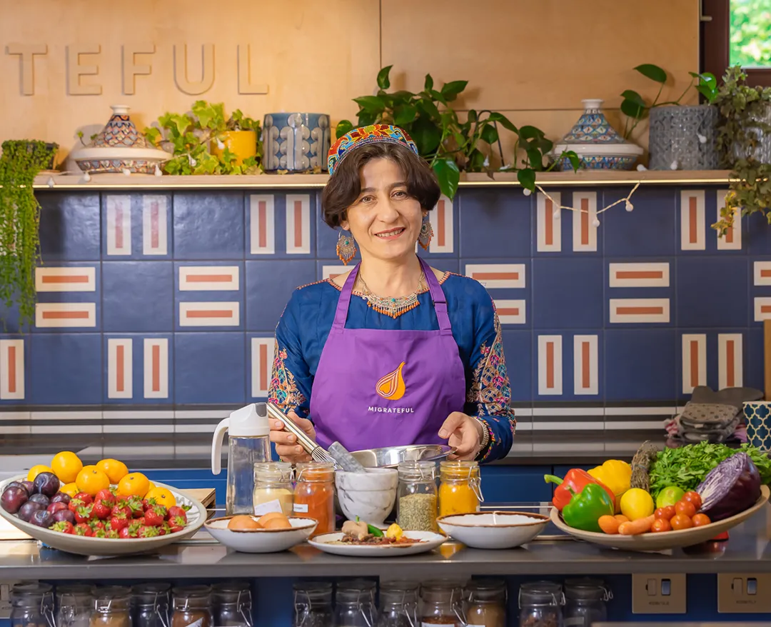A woman in an apron standing in front of a kitchen full of food at a London Cookery Class.