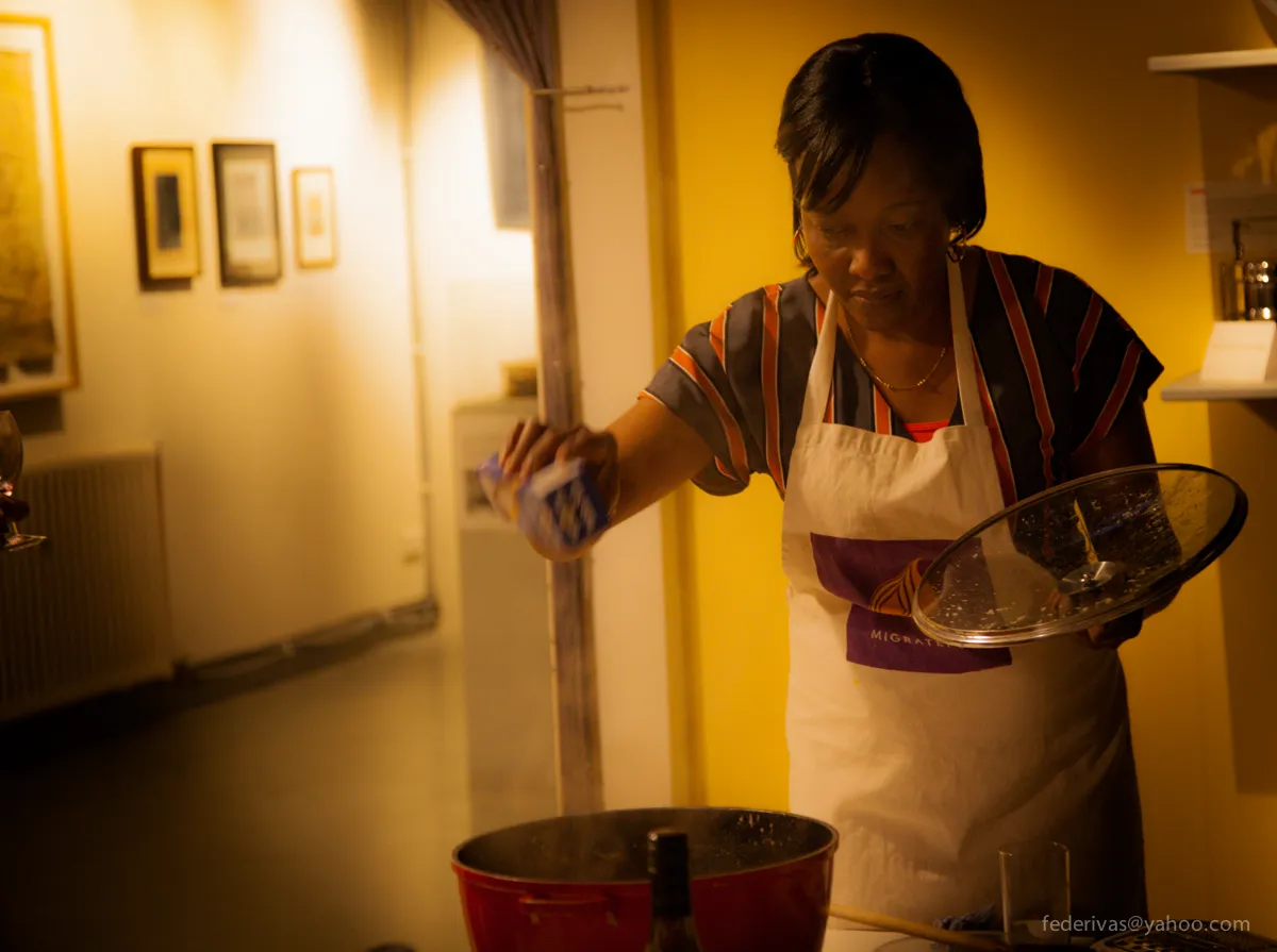 A Migrateful London Cookery Class participant, wearing an apron, skillfully pouring something into a pan.