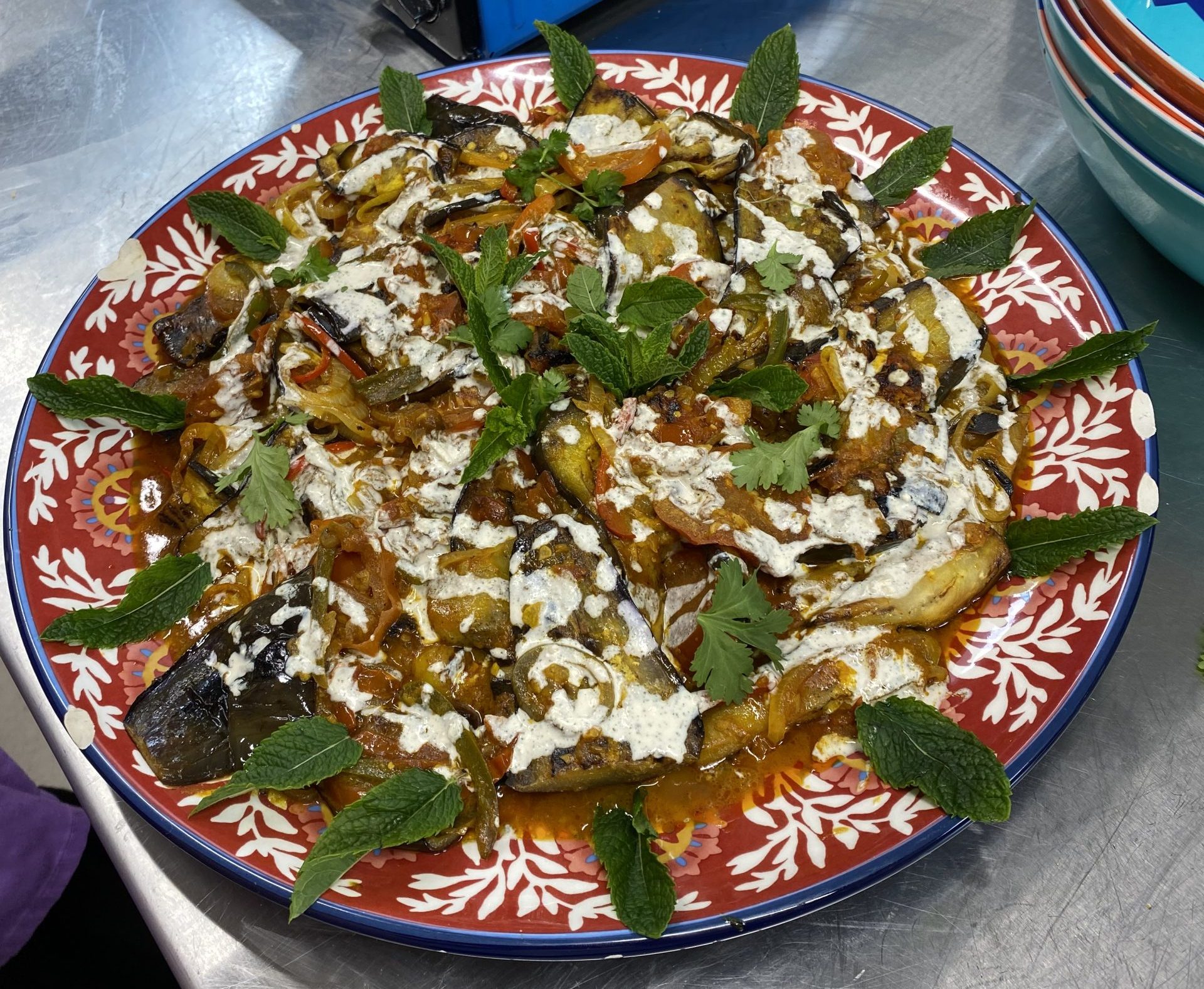 A patterned plate filled with aubergines decorated with yogurt and mint leaves.