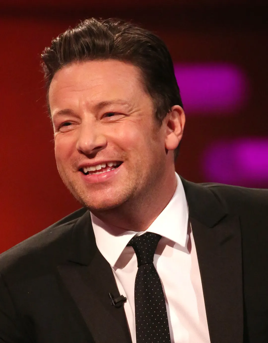 A man in a suit and tie smiling on the Graham Norton show, promoting Migrateful.