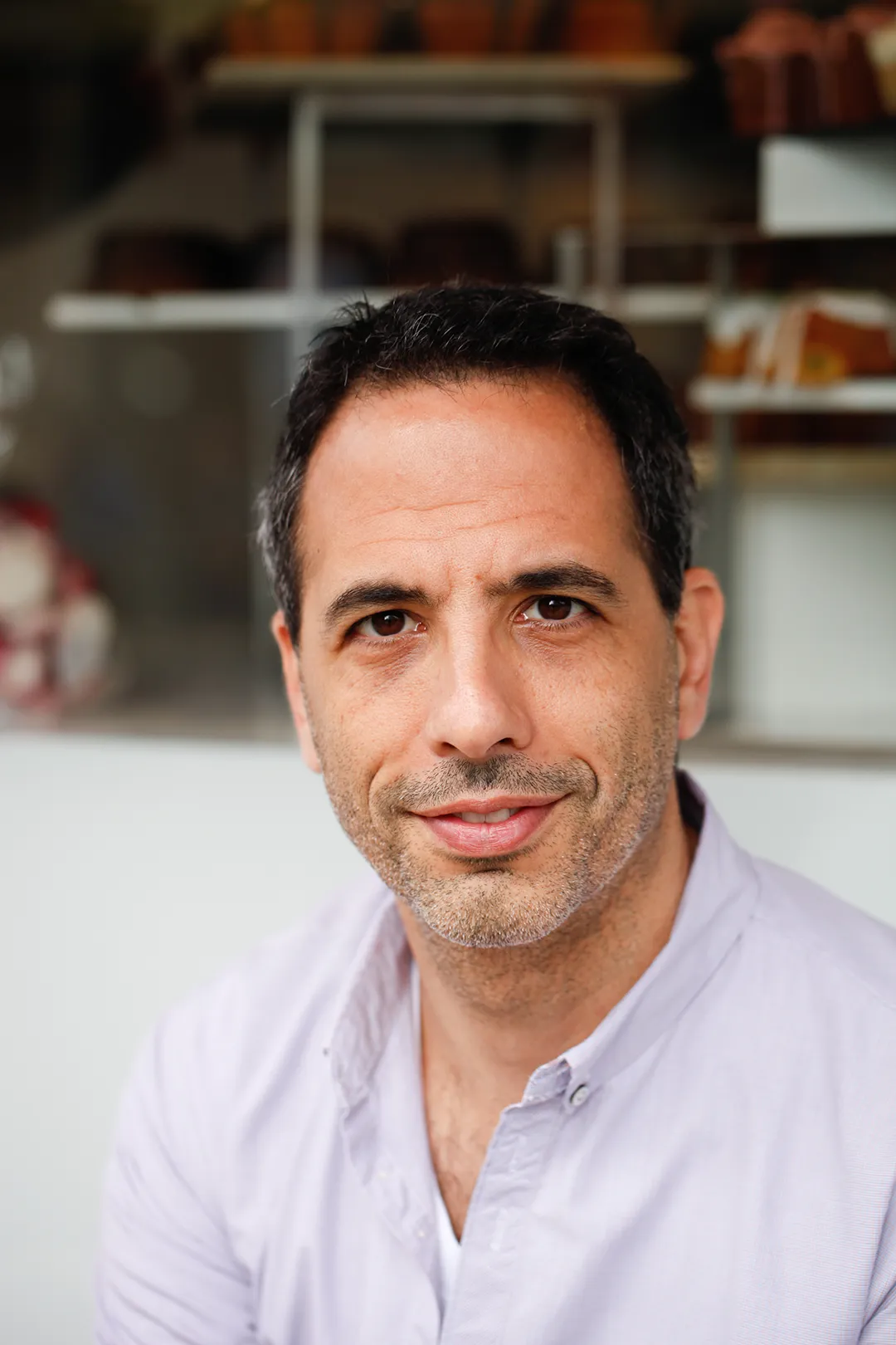 A man in a purple shirt sitting in front of a London bakery.