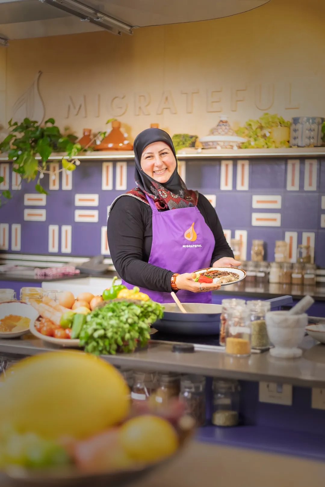 A Migrateful London Cookery Class instructor, donning an apron, stands confidently in front of a kitchen.