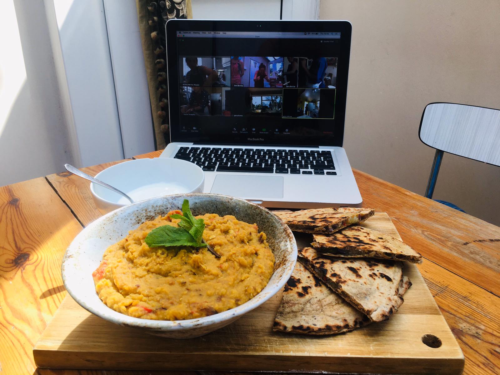 A bowl of curry and a plate of flatbread on a table in front of a laptop