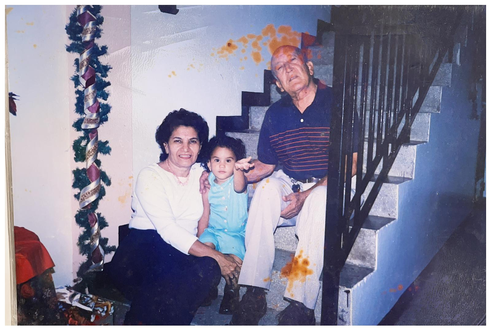 Gabi as a child (writer), and grandparents sit together on stairs beside a decorated railing with festive greenery. The mood is warm and familial, evoking a sense of nostalgia.