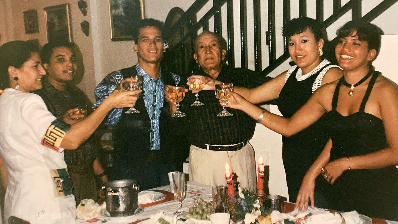 A family standing around a dining table, holding up glasses for a Christmas toast indoors.